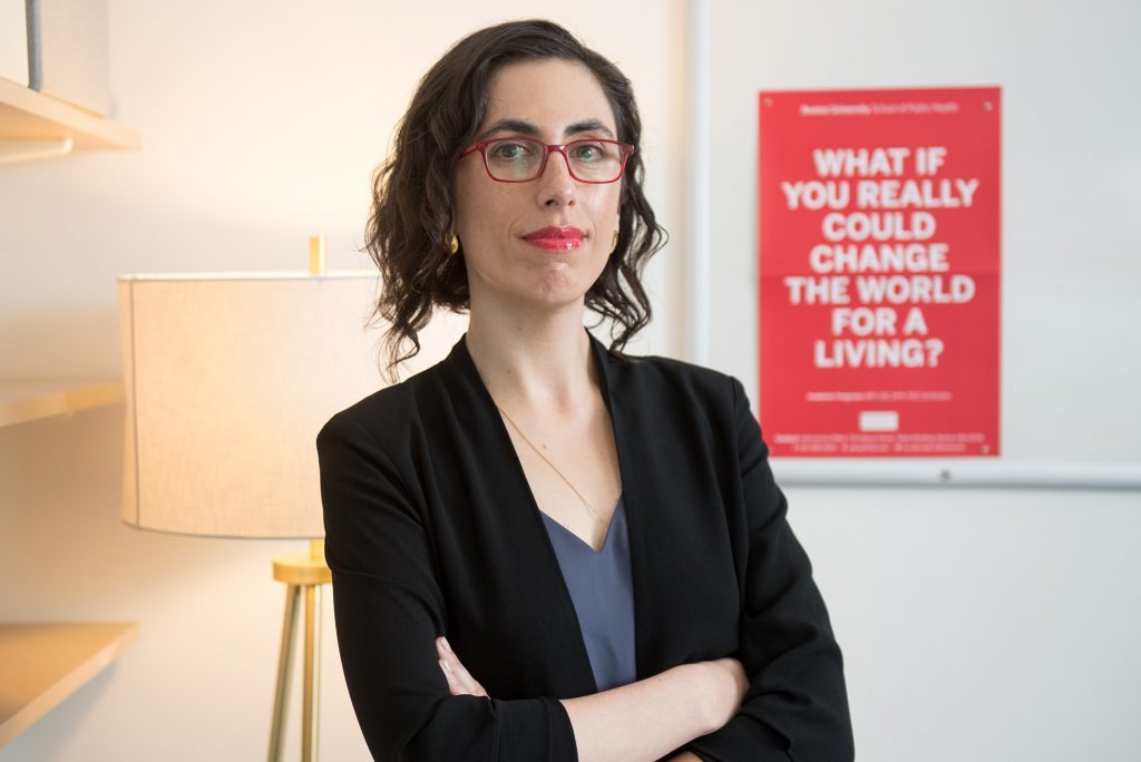 Sarah Lipson stands with arms crossed in front of a red posted that reads "What if you really could change the world for a living?"