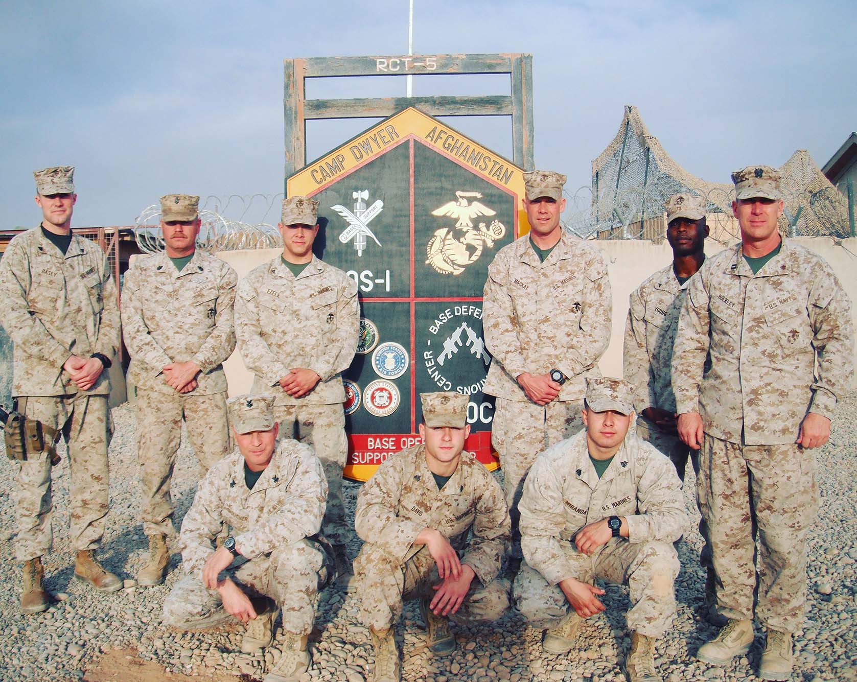 Photo of Edgar Miranda (squatting, far right) with fellow service members at Camp Dwyer in Afghanistan. They all wear a camouflage uniform and hat as they pose for a photo.